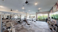 Located at 1348 Passenger St in Chattanooga, TN, this fitness center offers a generously sized, single-floor exercise space designed to accommodate a wide range of workout styles and fitness goals. The open floor plan is organized into distinct functional zones, each outfitted with professional-grade equipment. A dedicated strength training area features a multi-station cable and resistance rig, free weights including a full kettlebell rack, adjustable benches, and a climbing wall for functional fitness. The cardio zone is lined with large floor-to-ceiling windows that invite abundant natural light and offer views of the surrounding greenery, housing a row of treadmills and elliptical machines. Matrix-brand stationary bikes and spin cycles occupy their own section, complemented by motivational wall murals and inspirational typography that energize the space. A staircase connects to an upper-level area with additional cardio and cycling equipment, further expanding the workout capacity. Ceiling fans are distributed throughout, maintaining airflow and comfort. The interior is finished with durable patterned carpet tiles, recessed lighting, and a clean white palette that keeps the environment bright and modern. The overall ambiance is dynamic, functional, and purpose-built for serious fitness use.