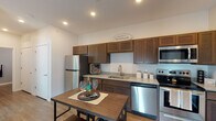 This single-floor residence offers a thoughtfully designed layout that balances comfort and functionality across its key living spaces. The kitchen is a standout area, featuring rich dark-walnut cabinetry extending to the upper walls, granite-look countertops, and a full suite of stainless steel appliances including a refrigerator, range, built-in microwave, and dishwasher. Wood-look luxury vinyl plank flooring runs throughout the main living areas, lending warmth and cohesion to the space. The living room is bright and welcoming, with a sliding glass door that allows natural light to fill the room and provides direct access to the outdoors. The primary bedroom features a distinctive teal accent wall, plush carpeting, and a ceiling fan, creating a calm and restful retreat. A second bedroom offers additional flexibility, with a large window that brings in ample natural light and carpet flooring. The bathroom is clean and practical, appointed with dark wood vanity cabinetry, a white countertop with an undermount sink, a large mirror with overhead lighting, and a shower-tub combination. Throughout the residence, neutral wall tones provide a versatile backdrop, while recessed lighting and modern fixtures contribute to a polished, contemporary feel.