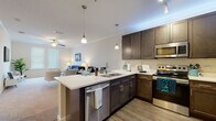 Located at 9611 Kona Village Dr in Riverview, FL, this single-floor residence offers a thoughtfully designed open-concept layout with modern finishes and a warm, welcoming ambiance. The kitchen is a standout feature, equipped with rich dark-wood cabinetry, stainless steel appliances including a refrigerator, range, and microwave, and a generous white quartz island with bar seating. Pendant lighting illuminates the space, which transitions seamlessly into the dining and living areas. The spacious living room is carpeted and bathed in natural light from large windows with blinds, and features crown molding and a ceiling fan overhead. Two well-sized bedrooms each offer plush carpeting, closet space, and windows that bring in ample natural light. Both bathrooms are finished with dark-wood vanities, white countertops, wood-look plank flooring, and large mirrors. The primary bathroom features a double-sink vanity, while the secondary bathroom includes a tub-shower combination. Throughout the residence, a consistent palette of neutral tones, wood-look flooring in the kitchen and bathrooms, and quality fixtures create a cohesive and refined living environment.