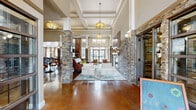 Located at 100 Heron Pointe Drive in Nashville, TN, this single-floor community clubhouse offers a generously sized and thoughtfully designed gathering space. The grand entrance foyer sets an impressive tone, featuring soaring double-height ceilings, a dramatic wrought iron chandelier, floor-to-ceiling windows, and stacked stone columns that carry throughout the interior, providing architectural continuity and a warm, lodge-inspired aesthetic.

The main lounge area is anchored by a stacked stone fireplace with a mounted television above, flanked by elegant seating arrangements atop decorative area rugs. Polished concrete floors in a rich amber tone flow seamlessly throughout, complementing the natural stone accents and warm lighting provided by pendant fixtures and coffered ceiling details.

A fully equipped kitchen features dark espresso cabinetry, granite countertops, a mosaic tile backsplash, and stainless steel appliances including a side-by-side refrigerator, range, microwave, and dishwasher. A dedicated coffee bar station adds everyday convenience for residents.

The billiards and game room offers a refined yet relaxed atmosphere, centered around a full-size pool table beneath a statement tray ceiling with geometric detail. Large windows dressed in warm drapery flood the room with natural light, while high-top dining seating completes the social setting.