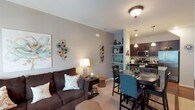 This single-floor residence offers a thoughtfully designed open-concept layout that seamlessly connects the living, dining, and kitchen areas. The living room features plush carpeting, neutral-toned walls, and large windows with vertical blinds that allow natural light to fill the space. The kitchen is outfitted with rich dark wood cabinetry, granite countertops, stainless steel appliances including a gas range, microwave, and refrigerator, and hardwood flooring that adds warmth underfoot. A breakfast bar with pendant lighting bridges the kitchen and dining area, creating an inviting space for casual meals. Built-in shelving provides additional display and storage options nearby.

The primary bedroom is a serene retreat, highlighted by a striking orb chandelier, soft carpeting, and windows dressed in light teal curtains that complement the room's calming palette. The second bedroom is equally comfortable, with ample natural light, carpeted floors, and a generously sized closet. Both bathrooms are finished with dark wood vanities, granite countertops, and hardwood flooring. One features a window for added ventilation and light, while the other offers a shower with tasteful decorative accents throughout. The overall ambiance is warm, cohesive, and move-in ready.