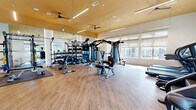 Located at 1609 W Chapman Dr in Sanger, TX, this dedicated fitness center offers a comprehensive workout environment designed for both cardio and strength training. The single-floor exercise room is generously proportioned, with soaring ceilings accented by a warm golden-yellow ceiling detail and sleek linear lighting that creates an energizing atmosphere throughout the space.

Large windows with roller shades line the walls, flooding the room with abundant natural light and providing views of the surrounding community. The durable light wood-tone flooring adds warmth and is practical for high-traffic use.

The cardio zone is well-appointed with multiple treadmills, a stair climber, and a stationary bike, all equipped with individual display screens. The strength training area features a multi-station cable machine, a full rack system, a weight bench, and a broad selection of dumbbells and free weights neatly organized along a mirrored wall — a thoughtful design choice that enhances the sense of space and allows users to monitor their form.

A standout decorative feature is the striking herringbone metallic tile accent wall, paired with a built-in wooden cubby storage unit — a stylish and functional touch. Locally inspired artwork and a Sanger-themed display add character and a sense of community pride to the space. Ceiling fans throughout ensure comfortable airflow during workouts.