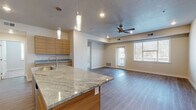 This well-appointed single-floor residence offers a thoughtfully designed open-concept layout that seamlessly connects the kitchen and living areas. The kitchen is a standout feature, showcasing flat-panel wood-tone cabinetry that extends to the ceiling for ample storage, granite countertops, and a full suite of stainless steel appliances including a range, over-the-range microwave, and refrigerator. A generous island with seating provides additional prep space and a casual dining option, illuminated by stylish pendant lighting overhead. The open living area is finished with durable wood-look plank flooring and features a ceiling fan, recessed lighting, and a door leading to an outdoor area, allowing natural light to fill the space. The bedrooms offer plush carpeting and natural light through blinds-covered windows, each with dedicated closet space featuring rod-and-shelf systems. The bathrooms are finished with the same granite and wood-tone vanity aesthetic as the kitchen, with one bathroom featuring a tub-shower combination and a connected walk-in closet area with laundry hookups. A second bathroom provides a tub-shower unit with clean white surround. Consistent use of neutral tones, modern fixtures, and cohesive materials throughout gives this residence a polished, contemporary feel.