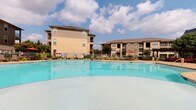 This residential community offers a well-appointed set of shared amenities designed for convenience and comfort. The outdoor pool area is a standout feature, presenting a generously sized, turquoise swimming pool surrounded by a clean, fenced deck with lounge seating and shaded areas with umbrellas. Mature landscaping lines the perimeter, and multi-story residential buildings frame the backdrop, creating an enclosed, resort-like atmosphere under open skies.

The interior mail center lobby showcases a contemporary design with soft blue-gray walls, light tile flooring, and a dark ceiling with recessed lighting that adds a polished contrast. Large floor-to-ceiling windows flood the space with natural light and offer views of surrounding greenery. Rows of bronze-finish individual mailboxes line both sides of a central island unit, which also features a package drop slot for added convenience. A series of framed geometric artworks adorns the walls, contributing a modern aesthetic. The overall ambiance of the lobby is clean, functional, and thoughtfully designed to serve residents efficiently.