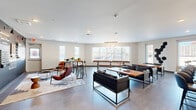 Located at 915 W Michigan St in Milwaukee, Wisconsin, this single-floor community space offers a thoughtfully designed open-concept layout combining a fully equipped kitchen and a spacious living and lounge area. The interior is finished with wide-plank hardwood-style flooring, neutral walls, and recessed lighting throughout, creating a clean and contemporary aesthetic.

The living area is generously sized and divided into distinct functional zones. A lounge section features sleek black leather sofas, a wood-topped coffee table, and accent chairs in warm cognac leather, anchored by layered area rugs. Adjacent to the lounge is a shuffleboard table beneath a striking cluster of globe pendant lights, adding a recreational focal point to the space. Large windows along the perimeter flood the room with natural light and offer views of the surrounding Milwaukee cityscape.

A bold accent wall finished in deep slate gray displays an array of mounted games and scoreboards, lending the space a social, activity-oriented character. Bar-height tables and seating provide additional gathering spots near the windows.

The kitchen is well-appointed with light wood cabinetry, a granite-topped island with bar seating, stainless steel appliances, and a slate tile backsplash. Distinctive hexagonal wall tiles and globe pendant lights add artistic flair. The overall ambiance is modern, welcoming, and purpose-built for community interaction.
