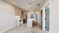 Located at 1100 Washington Ave in Golden, Colorado, this modern 2-bedroom, 2-bathroom unit offers a well-designed single-level layout with contemporary finishes throughout. The open kitchen serves as the heart of the home, showcasing light wood-tone cabinetry, white quartz countertops, a center island with an integrated sink and pendant lighting, stainless steel appliances including a French door refrigerator and range with a sleek wall-mounted hood, and a tile backsplash. Wood-look flooring runs through the kitchen and living areas, creating a warm, cohesive aesthetic. The two bedrooms are carpeted and filled with natural light from large windows offering views of the surrounding Golden neighborhood. Each bedroom features stylish panel doors with matte black hardware and access to closets. The bathrooms are finished with large-format tile flooring, wood-tone vanities, and a glass-enclosed walk-in shower. Additional conveniences include a dedicated laundry area, a pantry, and multiple closets for ample storage. The unit's neutral color palette, recessed lighting, and modern door and fixture details create a clean, move-in-ready atmosphere throughout.