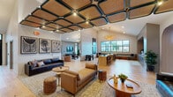 Located at 6615 Cerris Dr in Charlotte, NC, this thoughtfully designed single-floor space delivers a refined and welcoming atmosphere across a generously sized open floor plan. Light hardwood flooring flows seamlessly throughout, unifying the various areas and enhancing the sense of openness.

The living room is a standout centerpiece, boasting soaring vaulted ceilings that amplify the sense of volume and grandeur. Large floor-to-ceiling windows flood the space with natural light while offering views of the surrounding neighborhood. A dramatic geometric-patterned accent wall adds texture and visual interest, complemented by an elegant gold chandelier that serves as a striking focal point. Comfortable, curated seating arrangements create inviting conversation areas throughout.

Architectural arched doorways lend a timeless, sophisticated character to the space, framing transitions between zones. One area features a distinctive coffered ceiling with woven panel inserts, adding warmth and a boutique aesthetic. A built-in workstation nook with richly tiled backsplash and custom cabinetry provides a functional yet stylish workspace, while banquette seating along the windows offers additional versatility.

The hallway connects areas smoothly, maintaining the cohesive design language of warm neutrals, natural materials, and curated lighting. Overall, the space exudes a modern yet approachable elegance suited for community gathering and daily living.
