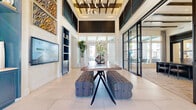 Located in Rancho Cucamonga, CA, this generously sized single-floor space offers an impressive blend of contemporary design and functional versatility. The grand entrance area immediately commands attention with its soaring ceilings adorned with exposed wood beam detailing and a striking chandelier, while large-format light tile flooring extends throughout, creating a cohesive and airy feel.

Floor-to-ceiling steel-frame glass walls and partitions define the architecture, allowing natural light to flow freely between zones while maintaining a sense of visual openness. The main living area features built-in navy cabinetry, wall-mounted displays, and curated artwork, lending the space a polished, sophisticated character.

The kitchen is outfitted with sleek gray cabinetry, a stone-topped waterfall island, modern pendant lighting, and direct access to an outdoor view, balancing style with practicality. A dedicated dining room offers a refined setting with a dark conference-style table, patterned carpeting, exposed beam ceilings, and access to outdoor views through expansive windows.

A secondary lounge area showcases rich herringbone hardwood flooring, teal accent walls, and floor-to-ceiling windows overlooking a pool area. Additional rooms include a private meeting room and an intimate lounge nook, each thoughtfully designed with ample natural light and curated furnishings throughout.