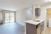 This single-floor residence offers a clean, modern aesthetic throughout, with light-toned luxury vinyl plank flooring, neutral walls, and textured ceilings that lend a cohesive, contemporary feel to every room. The open-concept layout connects the living area to the kitchen, creating an airy and functional space ideal for everyday living. A large sliding glass door in the living area fills the room with natural light and provides a view of lush greenery, while vertical blinds offer privacy and light control.

The kitchen is thoughtfully designed with gray shaker-style cabinetry, a white countertop peninsula with an undermount sink, and a full suite of stainless steel appliances including a refrigerator, range, microwave, and dishwasher. A dedicated laundry area is conveniently accessible directly from the kitchen, housing a full-size washer and offering added day-to-day practicality.

The bedroom is a calm, well-proportioned room with warm wood-toned flooring, recessed lighting, and ample wall space. The bathroom features a gray vanity with a white countertop, a framed mirror, and a full tub-shower combination, maintaining the same refined, neutral palette found throughout the residence. Together, these spaces form a well-balanced and move-in-ready home.