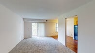 Located at 1187 Hillside Ave in Schenectady, NY, this single-floor unit offers a well-organized layout with a practical kitchen, generous living spaces, two bedrooms, and two bathrooms. The kitchen is equipped with light maple cabinetry, black appliances including a gas range, built-in microwave, dishwasher, and refrigerator, complemented by hardwood flooring that adds warmth to the space. The open living and dining area features plush wall-to-wall carpeting and is filled with natural light from a sliding glass door fitted with vertical blinds that opens to an outdoor area, as well as an additional side window offering pleasant exterior views. The two bedrooms are carpeted and well-sized, each with windows that bring in natural light and views of the surrounding grounds. Two bathrooms serve the unit: one features a walk-in glass-door shower with tile surround and a vanity with under-sink storage, while the second includes a full tub-shower combination with tile walls and tile flooring. The overall aesthetic is clean and neutral, with white walls throughout, creating a bright and welcoming atmosphere well-suited for comfortable everyday living.