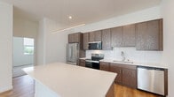 Located at 4300 W Brown Deer Rd in Brown Deer, Wisconsin, this well-designed single-floor residence offers 2 bedrooms and 3 bathrooms with a bright, contemporary aesthetic. The open-concept kitchen and living area serves as the heart of the home, featuring rich dark-stained cabinetry, stainless steel appliances, a white quartz countertop island with pendant lighting, and a subway tile backsplash. Light hardwood flooring flows throughout the main living areas, reflecting natural light from multiple windows that illuminate the clean white walls. The spacious living room provides an airy, open feel with ample room for a variety of layouts. Both bedrooms are carpeted for comfort, with the primary bedroom offering a generous footprint and easy access to the hallway. The three bathrooms are finished with wood-toned vanities, white quartz countertops, and clean, modern fixtures, including a walk-in shower with chrome hardware. A dedicated utility room and closet provide practical storage solutions. The home's layout is efficient and well-organized, connecting all rooms through a central hallway. Overall, the space presents a clean, modern living environment with a neutral palette and quality finishes throughout.