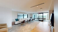 Located in Atlanta's prestigious Buckhead neighborhood, this professionally designed workspace offers a sophisticated and functional environment across a single, well-appointed floor. The layout is thoughtfully organized to balance private focus areas with collaborative gathering spaces.

The hallway serves as a polished transition zone, featuring warm light oak hardwood flooring, textured wallcoverings, and sleek black-framed glass doors that maintain visual connectivity while preserving acoustic separation between spaces.

The dining area functions as a versatile lounge and collaborative hub, furnished with a long banquette sofa, modular tables, and upholstered chairs in muted tones of navy and warm brown. Patterned carpeting adds texture underfoot, and large windows allow natural light to filter through to the seating area.

The living room serves as the primary meeting and conference zone, highlighted by a floor-to-ceiling glass wall that frames sweeping views of the Atlanta skyline. A substantial conference table anchored by a brass linear pendant light sits at the center, complemented by ergonomic task chairs. A wall-mounted display screen and dedicated workstation areas with built-in desks make this space equally suited for presentations and focused work. A private seating nook, accented by a bold teal feature wall, offers a quiet retreat for one-on-one conversations.