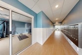 Located at 629 Old Liverpool Rd in Liverpool, NY, this single-floor amenity space offers a thoughtfully designed layout that balances comfort and functionality. The entrance welcomes visitors into a bright, open environment finished with warm wood-look flooring and a distinctive blue and white color palette carried throughout the hallways.

The hallways are a standout architectural feature, lined with dark wood lockers along one side and elegant white wainscoting on the other, leading toward large windows that flood the corridors with natural light and views of the surrounding outdoors.

The living room is a generously sized gathering area that immediately draws the eye with its bold gold-accented tray ceiling, plush carpeting, and an abundance of natural light streaming through large windows and glass doors that open to an outdoor balcony. The space is furnished with multiple seating arrangements — including a rich brown leather sectional, green upholstered sofas, and accent chairs — making it ideal for socializing or relaxing.

The exercise room, enclosed with glass walls and sliding doors, is well-equipped with cardio machines, a cable station, dumbbells, kettlebells, and floor mats, all set against the signature blue walls and carpeted flooring. Completing the space is a clean, functional bathroom featuring wood-look flooring and modern fixtures.