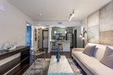 Located in the Parkwood Circle SE community in Atlanta, Georgia, this single-floor residence combines modern finishes with a warm, inviting atmosphere. The kitchen is a standout feature, outfitted with grey shaker-style cabinetry, granite countertops, and a full suite of stainless steel appliances including an electric range, microwave, and refrigerator. A peninsula with seating offers a casual dining option, while pendant lighting and a subway tile backsplash add contemporary style. Dark hardwood-style flooring runs throughout, providing a cohesive and elegant look. The bedroom is a relaxing retreat, featuring direct access to a private balcony through glass French doors that invite natural light and outdoor views. The room is generously proportioned and exudes a calm ambiance with neutral tones and warm accent lighting. The bathroom is finished with granite countertops on grey vanity cabinetry, tile flooring, and a full tub-shower combination with floor-to-ceiling tile surround. The overall design of this residence balances functionality and comfort, with thoughtful details and quality finishes throughout that create a refined, modern living environment.