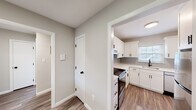 This single-floor unit combines modern updates with a functional, straightforward layout. The renovated kitchen serves as a standout feature, showcasing white shaker-style cabinetry with matte black hardware, light quartz countertops, and a subtle gray subway tile backsplash. Stainless steel appliances, including an electric range with an overhead ventilation hood and a dishwasher, complete the space. A window above the sink brings in natural light, while durable wood-style flooring ties the kitchen to the adjacent hallway and living areas seamlessly.

The entry and hallway areas feature the same wood-style flooring and neutral gray-toned walls, creating a cohesive aesthetic. A half-wall pass-through connects the living space to the kitchen, enhancing openness. The entry is anchored by a warm-toned wood door, adding a welcoming contrast to the lighter interior palette.

The bedrooms are finished with plush carpeting and neutral walls, each featuring windows that allow natural light and outdoor views. Baseboard heaters run along the perimeter of multiple rooms, providing consistent warmth. The bathroom includes a tiled tub-shower surround in clean white, complemented by a privacy window. Overall, the unit presents a clean, updated, and comfortable living environment.