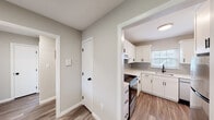 This single-floor unit combines modern updates with a functional, straightforward layout. The renovated kitchen serves as a standout feature, showcasing white shaker-style cabinetry with matte black hardware, light quartz countertops, and a subtle gray subway tile backsplash. Stainless steel appliances, including an electric range with an overhead ventilation hood and a dishwasher, complete the space. A window above the sink brings in natural light, while durable wood-style flooring ties the kitchen to the adjacent hallway and living areas seamlessly.

The entry and hallway areas feature the same wood-style flooring and neutral gray-toned walls, creating a cohesive aesthetic. A half-wall pass-through connects the living space to the kitchen, enhancing openness. The entry is anchored by a warm-toned wood door, adding a welcoming contrast to the lighter interior palette.

The bedrooms are finished with plush carpeting and neutral walls, each featuring windows that allow natural light and outdoor views. Baseboard heaters run along the perimeter of multiple rooms, providing consistent warmth. The bathroom includes a tiled tub-shower surround in clean white, complemented by a privacy window. Overall, the unit presents a clean, updated, and comfortable living environment.