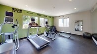 Located at 7400 Parkway Dr in La Mesa, California, this fitness center is a well-equipped, single-floor facility designed to support a well-rounded workout routine. The space features a bold and energizing aesthetic, highlighted by vivid green accent walls adorned with motivational typography decals — phrases like "When You're Tired, Stop When You're Done" and "Your Only Limit Is You" set an inspiring tone throughout.

The cardio section is outfitted with multiple treadmills, an elliptical trainer, and a stationary bike, each equipped with an individual display monitor. A dedicated free weights area includes a dumbbell rack with a range of weights and an adjustable workout bench, catering to strength training needs. A stability ball and a weight bench add further versatility for functional fitness exercises.

A large floor-to-ceiling mirror spans one wall, enhancing the sense of openness and allowing users to monitor their form during workouts. The durable, dark rubber flooring provides both safety and comfort underfoot.

Natural light flows in through multiple windows, offering views of the surrounding La Mesa neighborhood. Recessed ceiling lighting ensures consistent illumination throughout the space. The overall ambiance is clean, functional, and motivating — ideal for residents looking to maintain an active lifestyle.