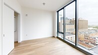 Located on the 12th floor of 801 N Orange Street in downtown Wilmington, Delaware, Studio 1203 is a thoughtfully designed studio that combines contemporary finishes with an efficient, open layout. Light hardwood flooring runs throughout the space, complementing the bright white walls and clean modern aesthetic.

The combined kitchen and living area serves as the heart of the studio. The kitchen features gray flat-front cabinetry extending to the ceiling for ample storage, a white quartz peninsula countertop ideal for dining or prep work, stainless steel appliances including a refrigerator, range, microwave, and dishwasher, and a stainless steel undermount sink. The open living area flows naturally from the kitchen toward expansive floor-to-ceiling windows framed in black, offering sweeping elevated views of the Wilmington cityscape.

The bathroom is finished with large-format marble-look porcelain tile surrounding a full soaking tub and shower combination, gray tile flooring, a light wood vanity, and recessed lighting, creating a clean and polished retreat.

Throughout the unit, the high-floor positioning maximizes natural light and provides unobstructed panoramic views of downtown Wilmington and beyond, making this studio a well-appointed urban residence in the heart of the city.