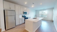 This 1-bedroom, 1-bathroom residence offers a thoughtfully designed layout across two floors, combining modern aesthetics with functional living spaces. The open-concept kitchen serves as the heart of the home, featuring crisp white shaker-style cabinetry extending to the ceiling for ample storage, stainless steel appliances including a refrigerator, electric range, and over-the-range microwave, and a large center island with a white quartz countertop and undermount sink. Light wood-tone flooring runs throughout the main living areas, complementing the bright, neutral color palette and recessed lighting overhead. Natural light flows in through multiple windows, offering views of the surrounding neighborhood. The spacious primary bedroom is finished with plush wall-to-wall carpeting and a generous window that fills the room with daylight. A dedicated walk-in closet provides substantial storage with wire shelving systems on multiple walls. The full bathroom features a white shaker vanity with quartz countertop, undermount sink, and brushed nickel hardware, maintaining the clean, contemporary style found throughout the residence. A connecting hallway ties the rooms together efficiently, contributing to an overall sense of comfort and practicality.