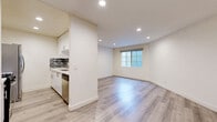 Located at 1221 N Orange Dr in the heart of Los Angeles, this one-bedroom, one-bathroom unit offers a well-organized layout across a single floor. The open-concept kitchen is equipped with white cabinetry, a stainless steel sink, a dishwasher, a stove, a microwave, and a refrigerator. A peninsula counter with a gray stone-style surface connects the kitchen to the dining and living areas, creating a functional and cohesive common space. Light wood plank flooring runs throughout the main living areas, lending a clean, modern aesthetic. The living room is highlighted by a charming fireplace with a white surround and large floor-to-ceiling windows that flood the space with natural light and offer open views of the surrounding Los Angeles skyline. The bedroom is a comfortable size, finished with plush carpeting and a wide window that brings in additional natural light and city views. A dedicated closet provides convenient storage. The bathroom features a combined shower and tub with sliding frosted glass doors, a toilet, and light wood-style flooring. Skylights in the kitchen provide additional ambient illumination. The overall design is bright and neutral, with white walls throughout creating a clean, inviting atmosphere.