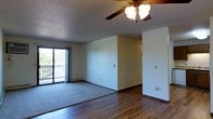 This single-floor residence offers a well-proportioned open living area that combines functionality with comfortable design. The main living space features a combination of warm hardwood-style flooring and plush carpeting, creating distinct zones within the room. A ceiling fan with an integrated light fixture is centrally mounted on the textured ceiling, providing both air circulation and ambient lighting throughout the space.

One of the standout features of the living area is the large sliding glass door, which floods the room with natural light and opens onto a private balcony enclosed by a classic white railing. The balcony provides views of the surrounding outdoor scenery, adding a sense of openness and connection to the outdoors.

The walls are finished in a neutral, light tone that enhances the brightness of the space and provides a versatile backdrop for a variety of interior styles. Baseboard heating is installed along the perimeter, ensuring efficient climate control throughout the cooler months. The clean, open layout of the living area allows for flexible furniture arrangement and makes the space feel airy and inviting. Overall, the residence presents a practical and comfortable living environment suited to a range of lifestyles.