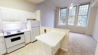 This single-floor, one-bedroom, one-bathroom unit is thoughtfully designed to maximize comfort and functionality. The open living area is expansive and airy, featuring tall ceilings, plush wall-to-wall carpeting, and a ceiling fan that enhances airflow and ambiance. Large multi-pane windows flood the space with abundant natural light and offer pleasant views of surrounding greenery, creating a bright and welcoming atmosphere.

The kitchen is fully equipped with white cabinetry, a white appliance suite including a refrigerator, electric range, and dishwasher, and ample counter space. A peninsula with a white countertop extends into the living area, serving as a convenient breakfast bar and providing a natural division between the kitchen and living spaces.

The bedroom is generously sized, carpeted for comfort, and features a ceiling fan and large windows that continue the home's bright, open character. A dedicated closet with a built-in rod offers practical storage. An additional nook or secondary space off the bedroom provides extra flexibility.

The bathroom is clean and straightforward, featuring a full tub-shower combination with white tile surround, a vanity with sink, and overhead lighting. Throughout the unit, the neutral color palette of soft whites and warm beiges contributes to a cohesive and calm aesthetic.