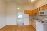 Located at 630 Water St in Santa Cruz, California, this one-bedroom, one-bathroom unit offers a thoughtfully organized single-floor layout that maximizes every square foot. The kitchen is outfitted with warm honey-toned wood cabinetry offering ample upper and lower storage, light countertops, and white appliances including an electric range, over-the-range microwave, and a full-size refrigerator. Light hardwood-style flooring runs throughout the kitchen and bathroom areas, lending a cohesive and clean aesthetic. The living room connects seamlessly to the kitchen and opens to a private balcony through a large window, allowing natural light to fill the space and providing pleasant outdoor views of surrounding greenery. The bedroom features neutral carpet flooring, bright white walls, and a dedicated closet for storage. The bathroom maintains the same warm wood tones found throughout, with a wood-framed vanity, integrated sink with light countertop, and hardwood-style flooring. Clean white walls throughout the unit create a bright, airy atmosphere. The overall ambiance is practical and welcoming, well-suited for comfortable single-occupant living in the heart of Santa Cruz.