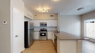 This single-floor residence offers a thoughtfully designed layout that balances functionality with modern style. The kitchen is a standout feature, equipped with stainless steel appliances including a refrigerator, electric range, and over-the-range microwave. Crisp white shaker-style cabinetry lines the walls, complemented by a light blue subway tile backsplash and dark quartz-style countertops that extend to a peninsula, providing additional workspace and storage. Light wood-tone luxury vinyl plank flooring runs throughout the kitchen and into the main living areas, adding warmth and easy maintenance.

The living area is generously proportioned and filled with natural light from a set of French doors flanked by windows, offering a view to the outdoors. A ceiling fan overhead enhances comfort. The entry area features neutral grey walls and a clean, open feel with the same light flooring extending seamlessly.

The bedroom is a quiet retreat with darker wood-tone vinyl plank flooring, neutral walls, and a ceiling fan. The bathroom includes a full soaking tub and shower combination with white tile surround and brushed nickel hardware. Throughout the space, neutral tones, consistent flooring, and modern fixtures create a cohesive and move-in-ready living environment.