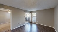 This efficient one-bedroom, one-bathroom unit is thoughtfully laid out across a single floor, offering a practical and comfortable living arrangement. The living room serves as the heart of the space, featuring rich, dark hardwood-style flooring that runs throughout the main living areas. Natural light fills the room through a sliding glass door that opens to a private balcony, accompanied by an additional window that frames outdoor views. A textured ceiling adds a classic finishing detail to the living area. The entry area shares the same durable flooring and opens seamlessly into the rest of the unit. The kitchen is equipped with white cabinetry, light-toned countertops, and an electric range, providing all the essentials in a compact, functional layout. The bedroom offers a carpeted floor for added comfort, a ceiling fan with light fixture, and a window that brings in natural light. A dedicated closet provides storage adjacent to the bedroom. The bathroom features a vanity with a speckled countertop and large mirror, a tiled tub surround, and a grab bar, delivering clean and practical finishes throughout. Neutral warm-gray wall tones unify the space, creating a cohesive and understated aesthetic throughout the entire unit.