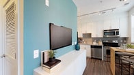 Located at 1717 E Capitol St SE in Washington, DC, this single-floor residence combines modern design with thoughtful functionality. The open-concept living and kitchen area is anchored by a bold teal accent wall, wood-look flooring, and track lighting that illuminates the space with a clean, contemporary feel. The kitchen is well-appointed with floor-to-ceiling white cabinetry, granite countertops, and a full suite of stainless steel appliances, including a refrigerator, electric range, microwave, and dishwasher. A dining area with a butcher block table sits adjacent to the kitchen, with a window providing natural light. The living room offers a relaxing retreat with deep teal walls, large windows that frame views of the surrounding neighborhood, and warm wood flooring underfoot. The bedroom is a calm, neutral-toned space featuring soft carpeting, natural light from double windows dressed with sheer curtains, and ample room for furnishings. The bathroom is finished with large-format tile flooring, granite vanity countertops, white cabinetry, and a shower-tub combination. A louvered utility closet in the hallway provides convenient in-unit storage. Throughout, the residence maintains a cohesive, modern aesthetic with carefully chosen finishes and an inviting ambiance.