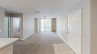 This single-floor residence offers a thoughtfully designed open-concept layout that seamlessly connects the main living areas. The kitchen is a functional galley-style space outfitted with crisp white shaker cabinetry, light marble-patterned countertops, and a full suite of black and stainless steel appliances, including an electric range, built-in microwave, refrigerator, and dishwasher. A double-basin stainless steel sink sits along the kitchen peninsula, which also provides a natural transition into the main living area. Open shelving adds an additional storage element near the kitchen's end.

The living area is generously sized, featuring neutral-toned carpet that extends throughout, complemented by tile flooring at the entryway. A ceiling fan provides overhead comfort, while a large sliding glass door floods the space with natural light and offers access to an outdoor balcony with views of surrounding greenery. Built-in shelving flanks the living area wall, providing convenient display or storage space.

The bathroom is clean and well-lit, featuring a marble-patterned vanity countertop, a framed mirror with an illuminated vanity light, white cabinetry, and a full tub-shower combination with white tile surround. Overall, the space presents a neutral, move-in-ready aesthetic with consistent finishes throughout.