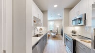 This thoughtfully designed one-bedroom, two-bathroom unit maximizes its compact footprint through an efficient, modern layout. The galley-style kitchen serves as a central feature, showcasing two-tone cabinetry with white upper cabinets and gray lower cabinets, white quartz countertops, a subway tile backsplash, and a full suite of stainless steel appliances including a range, microwave, dishwasher, and refrigerator. Light wood-look flooring runs throughout the main living areas, enhancing the bright, neutral color palette.

The open living area connects seamlessly to the kitchen, providing a functional space accented by recessed lighting and clean white walls. A window brings in natural light, creating an airy atmosphere despite the efficient scale of the space.

The generously proportioned primary bedroom accommodates a full furniture arrangement and features multiple windows that invite abundant natural light and outdoor views. A ceiling fan adds comfort, and the room connects to a walk-in closet with multi-tiered shelving and hanging rods on three walls, offering notable storage capacity.

The primary bathroom includes a gray vanity with quartz countertop, a glass-enclosed shower, and tile flooring consistent with the unit's modern aesthetic. The overall design is clean, cohesive, and well-appointed throughout.