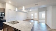Located in Vineyard, Utah, this well-designed one-bedroom, one-bathroom unit offers a smart, open-concept floor plan that maximizes every square foot. The kitchen serves as a central hub of the space, featuring a large granite-topped island with a double stainless steel sink, rich dark wood cabinetry, matching granite countertops along the perimeter, and black appliances including a refrigerator and range. Pendant lighting above the island adds a modern touch. The kitchen flows seamlessly into the open living area, which is finished with durable wood-look flooring and benefits from natural light through a set of front-facing double doors with windows. The spacious bedroom is carpeted for comfort and includes a walk-in closet with a built-in hanging rod, offering practical storage. A window in the bedroom frames views of the surrounding neighborhood. The bathroom is clean and functional, appointed with a dark wood vanity, granite countertop, a large mirror, and a full shower/tub combination. Wood-look flooring continues throughout the bathroom, tying the space together. Crisp white walls and consistent finishes give the entire unit a bright, cohesive, and move-in-ready feel.