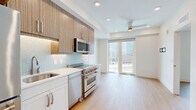 Located at 801 E Whiting St in the heart of downtown Tampa, FL, this thoughtfully designed one-bedroom, one-bathroom unit makes excellent use of its compact footprint across a single floor. Light-toned hardwood-style flooring flows consistently throughout the living areas and bedroom, creating a cohesive and clean aesthetic. The entry foyer welcomes residents with crisp white walls, a built-in ledge shelf, and a modern keypad-secured door. The well-appointed kitchen is a standout feature, showcasing wood-grain upper cabinetry, white lower cabinets, a decorative teal tile backsplash, white quartz countertops, and a full suite of stainless steel appliances including a French door refrigerator, electric range, built-in microwave, and dishwasher. Recessed lighting keeps the kitchen bright and functional. The bedroom is a serene, minimalist space highlighted by a dramatic floor-to-ceiling window that frames sweeping views of the Tampa downtown skyline and cityscape, flooding the room with natural light. The bathroom features elegant large-format hexagonal marble-look tile flooring, a vanity with multi-drawer storage, and clean white walls, lending a polished, contemporary feel. Overall, the unit offers a modern urban living experience with refined finishes throughout.