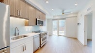 Located at 801 E Whiting St in the heart of downtown Tampa, FL, this thoughtfully designed one-bedroom, one-bathroom unit makes excellent use of its compact footprint across a single floor. Light-toned hardwood-style flooring flows consistently throughout the living areas and bedroom, creating a cohesive and clean aesthetic. The entry foyer welcomes residents with crisp white walls, a built-in ledge shelf, and a modern keypad-secured door. The well-appointed kitchen is a standout feature, showcasing wood-grain upper cabinetry, white lower cabinets, a decorative teal tile backsplash, white quartz countertops, and a full suite of stainless steel appliances including a French door refrigerator, electric range, built-in microwave, and dishwasher. Recessed lighting keeps the kitchen bright and functional. The bedroom is a serene, minimalist space highlighted by a dramatic floor-to-ceiling window that frames sweeping views of the Tampa downtown skyline and cityscape, flooding the room with natural light. The bathroom features elegant large-format hexagonal marble-look tile flooring, a vanity with multi-drawer storage, and clean white walls, lending a polished, contemporary feel. Overall, the unit offers a modern urban living experience with refined finishes throughout.