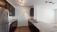 This well-appointed 1-bedroom, 1-bathroom unit in Jackson, Mississippi offers a thoughtfully designed single-floor layout with a blend of functional and modern finishes throughout. The kitchen is a standout feature, showcasing dark espresso cabinetry, granite-style countertops, a double-basin sink, and a full suite of stainless steel appliances including a refrigerator, built-in microwave, and electric range. Warm wood-style flooring runs throughout the kitchen and living areas, adding a cohesive and inviting aesthetic. The spacious bedroom is finished with plush wall-to-wall carpeting and features a ceiling fan with light fixture, a large window that allows for generous natural light, and access to a dedicated walk-in closet equipped with built-in wire shelving and hanging rods for ample storage. A second closet is also visible nearby, providing additional organization options. The full bathroom includes a combined tub and shower, toilet, and wood-style flooring that complements the rest of the unit. The overall layout, as seen in the dollhouse view, is efficiently arranged to maximize the use of space, creating a comfortable and practical living environment suited for single occupancy or a couple.