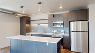 Located in the heart of downtown Salt Lake City, this well-appointed 1-bedroom, 2-bathroom residence offers a thoughtfully designed open-concept layout across a single floor. Warm hardwood-style flooring flows throughout, complementing the clean, contemporary aesthetic.

The combined living, dining, and kitchen area serves as the centerpiece of the home. Floor-to-ceiling windows flood the living space with natural light and frame impressive views of the Salt Lake City skyline and the surrounding Wasatch Mountains. Exposed industrial ductwork and track lighting add an urban loft character to the airy living area.

The kitchen is a standout feature, showcasing dark wood cabinetry, a light blue tile backsplash, and a large waterfall-edge island with a quartz countertop—ideal for casual dining or entertaining. Stainless steel appliances, including a dishwasher, range, microwave, and refrigerator, complete the modern culinary setup. Pendant lighting accents the island overhead.

The spacious primary bedroom connects to a well-organized walk-in closet with ample shelving and hanging space, along with two additional closets for generous storage. Both bathrooms feature dark wood vanities, vessel or undermount sinks, LED-backlit mirrors, and light wood-tone flooring. An in-unit laundry area adds everyday convenience to this polished downtown residence.