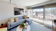 This thoughtfully designed one-bedroom, one-bathroom residence offers a smart and functional layout that maximizes every square foot. The open-concept living area features textured accent walls, exposed overhead ductwork lending an industrial-modern character, and large floor-to-ceiling windows that flood the space with natural light and provide sweeping street-level views of the surrounding neighborhood. The living room offers generous space for comfortable seating and flows seamlessly into the kitchen.

The kitchen is outfitted with crisp white cabinetry, sleek white countertops, and a full suite of stainless steel appliances including a refrigerator, electric range, and built-in microwave. Track lighting overhead adds both function and a modern aesthetic, while a U-shaped layout provides ample counter and storage space.

The bedroom is a tranquil retreat, featuring large windows with views of the outdoors, a ceiling fan, and exposed structural details consistent with the unit's industrial-modern design. A walk-in closet area provides additional storage.

The bathroom is clean and contemporary, featuring white cabinetry, a wide single-sink vanity with a large mirror, wood-look flooring, and a glass-enclosed shower. The in-unit washer and dryer hookup adds everyday convenience. Throughout the space, light-toned flooring and a bright, neutral color palette create a cohesive and inviting atmosphere.