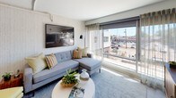 This thoughtfully designed one-bedroom, one-bathroom residence offers a smart and functional layout that maximizes every square foot. The open-concept living area features textured accent walls, exposed overhead ductwork lending an industrial-modern character, and large floor-to-ceiling windows that flood the space with natural light and provide sweeping street-level views of the surrounding neighborhood. The living room offers generous space for comfortable seating and flows seamlessly into the kitchen.

The kitchen is outfitted with crisp white cabinetry, sleek white countertops, and a full suite of stainless steel appliances including a refrigerator, electric range, and built-in microwave. Track lighting overhead adds both function and a modern aesthetic, while a U-shaped layout provides ample counter and storage space.

The bedroom is a tranquil retreat, featuring large windows with views of the outdoors, a ceiling fan, and exposed structural details consistent with the unit's industrial-modern design. A walk-in closet area provides additional storage.

The bathroom is clean and contemporary, featuring white cabinetry, a wide single-sink vanity with a large mirror, wood-look flooring, and a glass-enclosed shower. The in-unit washer and dryer hookup adds everyday convenience. Throughout the space, light-toned flooring and a bright, neutral color palette create a cohesive and inviting atmosphere.