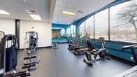 Located at 700 Stockton St in Richmond, VA, this single-floor fitness facility is designed to support a comprehensive range of workout modalities. The space is characterized by bold teal accent walls, durable rubber flooring throughout, and a suspended drop-tile ceiling with recessed fluorescent lighting that ensures consistent illumination across all areas.

The main workout floor is generously proportioned, offering ample room for strength training machines, cable systems, adjustable benches, and free weights including a dumbbell rack. A dedicated functional training zone features a multi-station power rack, battle ropes, and a heavy punching bag, providing versatile options for dynamic and high-intensity workouts. Full-length mirrors line portions of the walls, enhancing the sense of space and allowing users to monitor their form.

A glass-enclosed studio area, accessible via a full-height glass partition and door, houses exercise balls, suspension training equipment, and hardwood-style flooring — ideal for group sessions or personal training. Adjacent to this studio, a cardio zone benefits from floor-to-ceiling windows that flood the space with natural light and offer open views of the surrounding streetscape and mature trees, creating an energizing environment for treadmill and cycling workouts.

Overall, the facility presents a clean, organized, and professional atmosphere well-suited for a broad range of fitness activities.