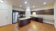 This single-floor residence in Minot, North Dakota offers a thoughtfully designed layout that balances open living spaces with comfortable private quarters. The heart of the home is a spacious open-concept kitchen and living area, where warm hardwood-style flooring flows throughout. The kitchen is well-equipped with rich dark espresso cabinetry, light granite-style countertops, a central island, black appliances including a range, microwave, and dishwasher, plus a stainless steel refrigerator. Recessed lighting illuminates the space, creating a bright and functional atmosphere. The living area transitions seamlessly from hardwood flooring to plush carpeting, with a sliding glass door that invites natural light and outdoor access. The bedrooms are carpeted and offer a calm, neutral palette, with ample closet space including a walk-in closet with wire shelving. The primary bathroom features a dual-sink vanity with dark wood cabinetry, a large mirror, and stone-look tile flooring. A second full bathroom includes a tub-shower combination, single vanity, and matching tile flooring. Throughout the home, clean white trim, panel doors, and a consistent design language create a cohesive and inviting living environment.