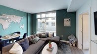 This single-floor residence showcases a thoughtfully designed interior with a contemporary aesthetic carried throughout each room. The living area is anchored by a large sectional sofa and features bold teal-painted walls, floor-to-ceiling windows that flood the space with natural light, and urban views of the surrounding streetscape. A decorative world map installation adds a distinctive artistic focal point to the room.

The kitchen is outfitted with dark espresso cabinetry extending to the ceiling, white quartz countertops, a subway tile backsplash, stainless steel appliances including a refrigerator, range, and microwave, and a peninsula with an undermount sink and pendant lighting above.

Two bedrooms offer individual character. One features a striking navy accent wall, wall-mounted sconce lighting, and a window with outdoor views. The other presents a neutral palette enhanced by a dramatic dark wood slat installation that extends from the headboard wall up toward the ceiling, creating a sculptural architectural element.

Both bathrooms are finished with light tile flooring and white surfaces. One includes a glass-enclosed walk-in shower with white tile surround and a dark vanity with white countertop, while the second features a full soaking tub with shower, a curtain rod, and ample closet storage nearby.