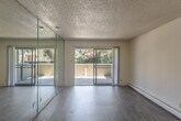 This 2-bedroom, 1-bathroom single-floor residence offers a practical and well-organized layout comprising a living room, kitchen, two bedrooms, a full bathroom, and a hallway. The living room is a standout space, featuring floor-to-ceiling mirrored wall panels that amplify natural light and create a sense of openness. Sliding glass doors lead directly to an outdoor balcony, framing views of lush surrounding greenery. Hardwood-style flooring runs throughout the living area, while a textured ceiling adds a classic residential character. A baseboard heating system is present throughout the unit. Adjacent to the living room, a dining area features hardwood-style flooring, a window for natural light, and a chandelier overhead. The kitchen is efficiently designed with white upper and lower cabinetry, a standard countertop with sink, and includes a range, dishwasher, and refrigerator. A side window brings in additional natural light. The primary bedroom offers hardwood-style flooring, a closet, and baseboard heating. The secondary bedroom is carpeted and features a window with garden views and a textured ceiling. The full bathroom includes a tiled tub-shower combination, toilet, and hardwood-style flooring. Both bedrooms are carpeted, offering a comfortable, quiet retreat.