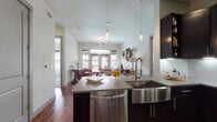 This single-story residence presents a thoughtfully designed open-concept layout that seamlessly connects the kitchen, dining, and living areas. The kitchen is a standout space, featuring rich dark espresso cabinetry extending to the ceiling, a stainless steel farmhouse sink, quartz countertops with a tile backsplash, under-cabinet lighting, and stainless steel appliances including a gas range and built-in microwave. Glass pendant lights hang above the central island, adding a refined touch. Rich hardwood flooring flows throughout the main living areas, leading into a bright living room with large windows and French doors that invite natural light and outdoor views. A ceiling fan anchors the space above comfortable seating.

The bedrooms feature plush carpeting, ceiling fans, and generous windows with roller shades. Both bathrooms are appointed with dual-sink vanities, dark cabinetry, quartz countertops, large mirrors, and tile flooring. One bathroom includes a tiled walk-in shower. A dedicated laundry area with full-size washer and dryer and overhead cabinetry adds practical convenience. The overall ambiance is modern yet warm, balancing sleek finishes with inviting design elements throughout.