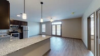 This single-story unit offers a thoughtfully designed open-concept layout where the kitchen flows seamlessly into the living area, creating a spacious and connected environment. The kitchen is well-appointed with rich, dark espresso cabinetry extending to the ceiling for ample storage, granite countertops, and a full suite of stainless steel appliances including a refrigerator, range, dishwasher, and microwave. A granite-topped island provides additional workspace and serves as a natural divider between the kitchen and living space. Pendant lighting hangs above the island, complementing the recessed lighting throughout the kitchen.

The living area is bright and open, featuring wood-look plank flooring, neutral-toned walls, and a ceiling fan. Natural light enters through multiple windows with blinds and a set of glass French doors that open to an exterior space. The bedroom features plush carpet flooring and a generously sized window. A walk-in closet with wire shelving offers well-organized storage. The bathroom includes a dual-sink vanity with granite countertops, dark cabinetry, paired mirrors, and stylish sconce lighting, maintaining a consistent, cohesive aesthetic throughout.