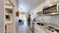 Located at 960 W Southern Ave in Mesa, Arizona, this one-bedroom, one-bathroom unit offers a thoughtfully designed layout that maximizes every square foot across a single floor. The kitchen features crisp white shaker cabinets with brushed nickel hardware, granite countertops, stainless steel appliances including a dishwasher, microwave, and refrigerator, all set atop wood-look plank flooring that runs throughout the unit. The spacious bedroom serves as the heart of the home, accommodating a full sleeping and sitting area with ease. A ceiling fan provides comfort, while a sliding glass door with white curtains opens to an outdoor access point, allowing natural light to fill the room. A wall-mounted A/C unit ensures year-round climate control. The bathroom is clean and functional, featuring a tub and shower combination with a white curtain, a granite-topped vanity with white cabinetry, a large mirror, and wood-look tile flooring that complements the rest of the unit. Neutral warm-gray tones on the walls create a cohesive, modern ambiance throughout, making this a well-appointed and efficient living space in the heart of Mesa.