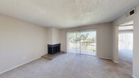 This single-floor, one-bedroom, one-bathroom unit offers a practical and comfortable layout across a compact yet efficiently designed floor plan. The entry opens into a hallway that transitions seamlessly between the living spaces, with wood-look flooring at the threshold giving way to plush carpet throughout the main living areas.

The combined kitchen and living room serves as the heart of the unit. The living area is highlighted by a raised-hearth fireplace with a dark surround, adding a cozy focal point to the room. A large sliding glass door fitted with vertical blinds fills the space with natural light and provides views of the surrounding greenery outside. The kitchen features a peninsula counter with a speckled laminate surface, warm wood-toned upper cabinets, a white electric range, a double-basin stainless steel sink, and a full-size refrigerator, all set on wood-look flooring.

The spacious primary bedroom is carpeted and includes a sliding closet and its own sliding glass door with vertical blinds, allowing for additional natural light and outdoor access. The bathroom is clean and functional, offering a full tub-shower combination with tile surround, a vanity with a speckled countertop, and wood-look flooring. A textured ceiling is consistent throughout the unit, completing the space.