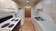 This single-floor residence offers a functional and straightforward layout with neutral finishes throughout. The open living area is generously sized, featuring light beige wall-to-wall carpeting and large sliding glass doors fitted with vertical blinds that allow natural light to fill the space. An adjoining area, also carpeted, provides additional flexible living space.

The galley-style kitchen is efficiently designed with white cabinetry lining both sides, offering ample upper and lower storage. A stainless steel sink, electric coil range, refrigerator, and dishwasher are included, while light wood-tone flooring ties the space together. A wood bi-fold door at the end of the kitchen leads to an adjacent area.

The bedroom is carpeted and features a large window with vertical blinds, providing natural light and outdoor views. A walk-in closet offers notable storage capacity alongside an additional door providing access to the hallway.

The full bathroom includes a single-sink vanity with white cabinetry, a wall mirror, and a tub-shower combination with white tile surround and light tile flooring. A dedicated laundry area houses a stacked washer and dryer unit with built-in shelving for added storage convenience.