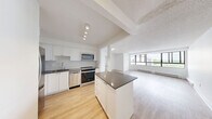 Located at 545 Belmont Ave W in Kitchener, Ontario, this well-appointed 2-bedroom, 1-bathroom unit offers a thoughtfully designed single-floor layout. The open-concept kitchen and living area form the heart of the home, highlighted by a central island with a dark stone countertop, white shaker-style cabinetry, a classic subway tile backsplash, and a full suite of stainless steel appliances including a refrigerator, electric range, built-in microwave, and dishwasher. Track lighting above the kitchen adds a modern, functional touch. Light-toned hardwood flooring flows seamlessly throughout the entire unit, lending warmth and continuity to every room. The spacious living area is bathed in natural light through a wide bank of floor-to-ceiling windows that frame sweeping treetop views — a standout feature of the space. Both bedrooms are comfortably sized with clean white walls and continued hardwood flooring, offering a bright and neutral canvas. The bathroom is elegantly finished with white subway tile surrounding the soaker tub and shower, a dark wood vanity with a white countertop, tile flooring, and a large mirror. A dedicated closet provides practical storage. The overall aesthetic is clean, modern, and move-in ready.