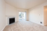 Located at 11240 NE 132nd St in Kirkland, Washington, this two-bedroom, single-floor residence offers a well-organized layout designed for comfortable everyday living. The living room serves as the heart of the home, featuring plush carpeting, a classic tile-surround fireplace with a white wood mantle, and sliding glass doors that open to a private patio, allowing for abundant natural light and easy outdoor access. Adjacent to the living area, the kitchen is thoughtfully designed in a galley style, outfitted with white shaker-style cabinetry, granite-look countertops, a white appliance suite, and tile flooring. A breakfast bar connects the kitchen to the main living area, enhancing the open feel of the shared space. A hallway leads to two well-proportioned bedrooms, each finished with soft carpeting, natural light from window-mounted blinds, and ample closet space with reach-in configurations. The bathroom features a full tub-shower combination with clean white surround panels and tile flooring. Throughout the residence, neutral tones and consistent finishes create a cohesive and move-in ready environment. Baseboard heating is present in the bedrooms, ensuring year-round comfort in the Pacific Northwest climate.